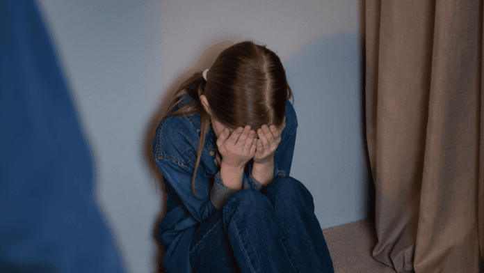 Criança sentada no chão cobrindo o rosto