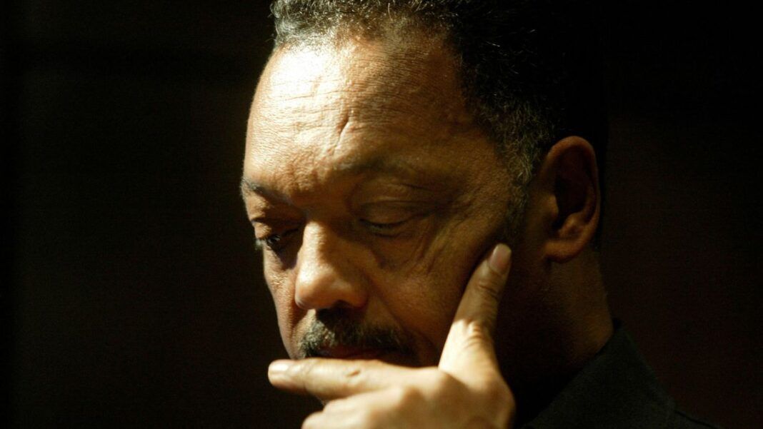 Close-up do rosto de um homem negro de cabelos grisalhos e bigode. Ele está com os olhos baixos, expressão séria e pensativa, com o dedo indicador encostado no queixo. O fundo está escuro e a iluminação foca em seu rosto.