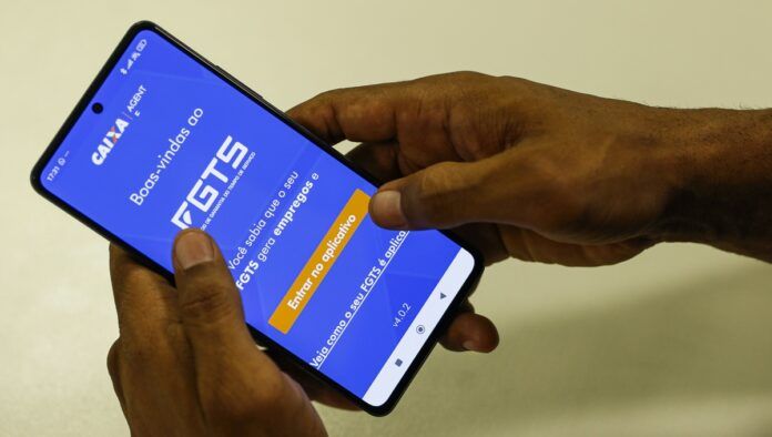 Mão segura celular com aplicativo do FGTS na tela