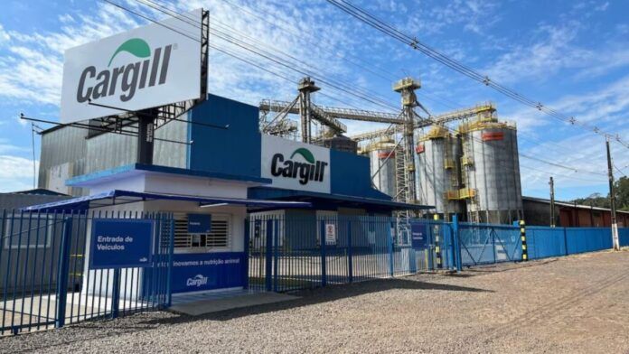 Vista externa de uma unidade industrial da Cargill sob um céu azul com nuvens esparsas. Em primeiro plano, há uma guarita branca e azul com uma placa indicando 